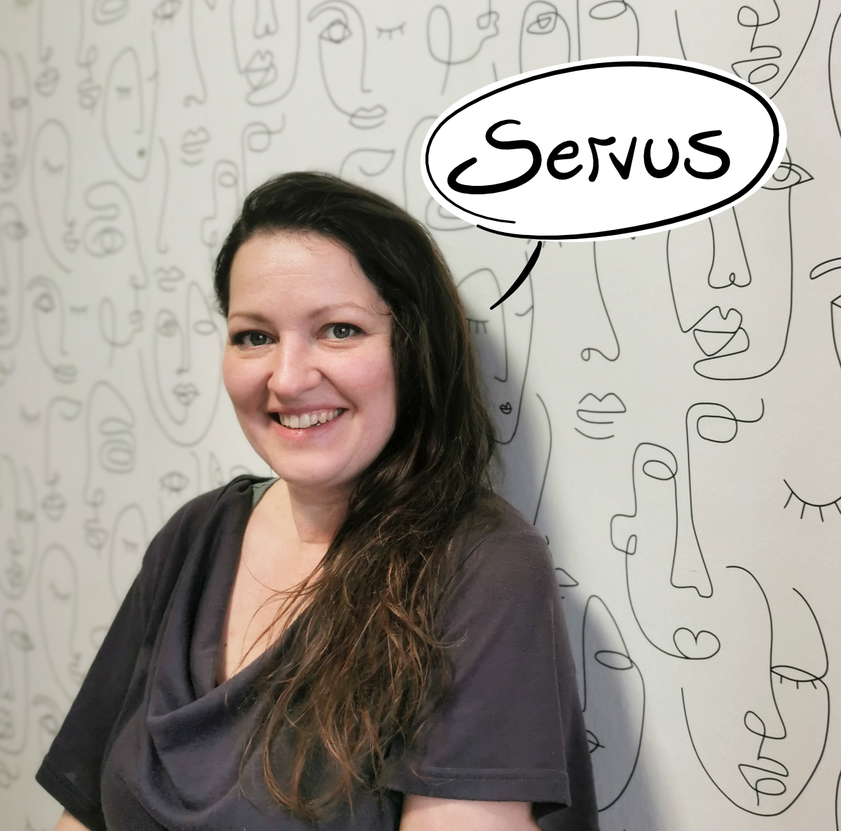 Andrea Eigler, Grafikerin und Illustratorin aus dem Bezirk Wiener Neustadt, lächelt vor einer Tapete mit Linienzeichnungen – mit handgezeichneter Sprechblase „Servus".