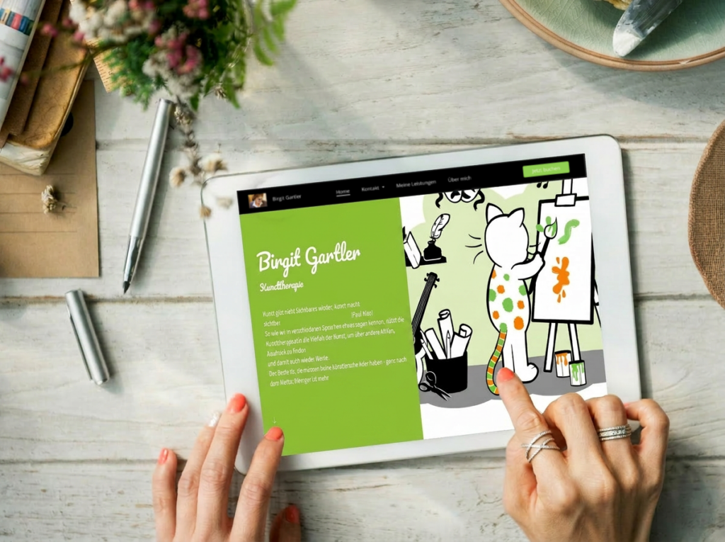 Tablet-Mockup der Website von Birgit Gartler Kunsttherapie – mit handgezeichneter Katzenfigur als Maskottchen beim Malen vor einer Staffelei, auf grünem Hintergrund.