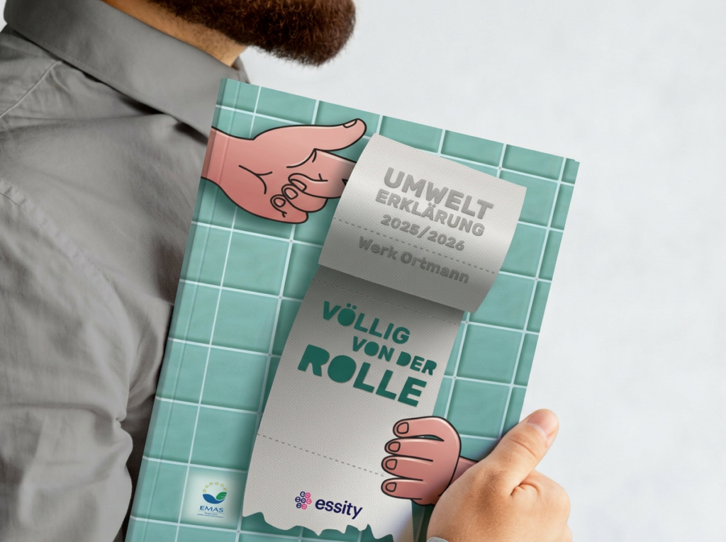 Person hält die Essity Umwelterklärung 2025/2026 in den Händen – Cover mit Klopapierrolle auf Badezimmerfliesen-Hintergrund und dem Titel „Völlig von der Rolle".
